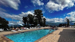 Ein Schwimmbecken mit Liegestühlen und Sonnenschirmen, umgeben von Bäumen und blauem Himmel.