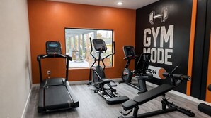 Ein Fitnessraum mit Laufband, Crosstrainer und einer Gewichtbank.