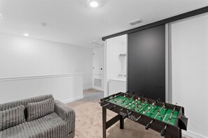 A room with a foosball table, a gray sofa, and a white radiator. - Elegant Home near Disney - pool - free parking (Kissimmee)