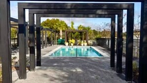 Ein Pool mit einer Holz-Pergola, umgeben von einem gepflasterten Gehweg.