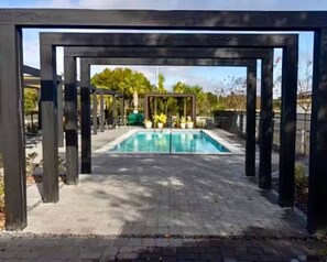 A swimming pool with a wooden pergola structure, surrounded by a paved walkway. - Elegant Home near Disney - pool - free parking (Kissimmee)
