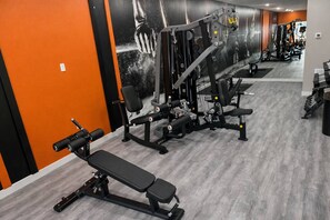 Uma academia com equipamentos de ginástica, bancos e um espelho grande na parede.