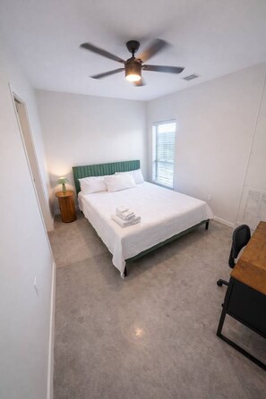 Een slaapkamer met een bed, een plafondventilator, een nachtkastje met lamp en een raam.