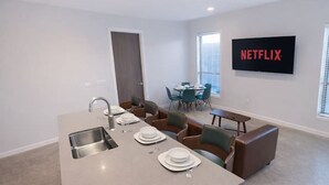 Moderni keittiö, jossa on keskeinen saareke, ruokailutila tuoleineen, sohva ja televisio, jonka näytöllä näkyy Netflixin logo.