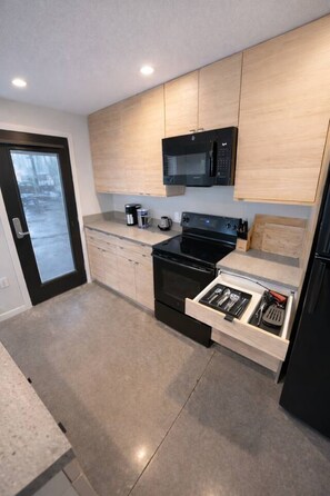 Een moderne keuken met een magnetron, oven en een ingebouwde lade met keukengerei.