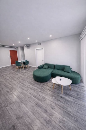 A modern living room with a sectional sofa, a round coffee table, and a dining area with chairs and a table. - Three Bedroom Unit in Des Moines (Des Moines)