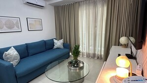 A modern living room with a blue sofa, a glass coffee table, and a white air conditioning unit. - Apartment in the center of Santo Domingo. Steps away from the main roads. (Santo Domingo)