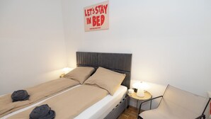 A double bed with two pillows, a bedside table with a lamp, and a chair.