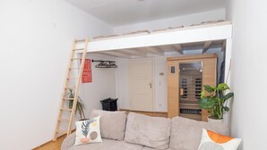 A modern living room with a beige sectional sofa, a wooden ladder, a potted plant, and a wooden cabinet.