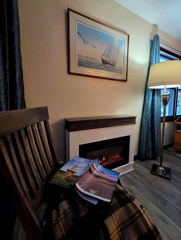 A cozy room with a fireplace, a framed seascape painting, and a table with travel brochures.
