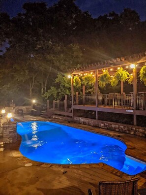 A swimming pool with a pergola and string lights, surrounded by trees. - Pool House Group (Chattanooga)