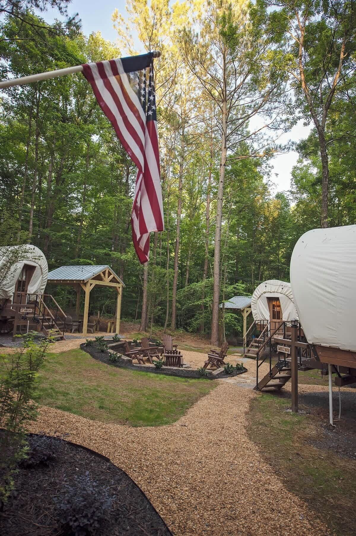 Ein Campingplatz mit überdachten Bereichen, einem Fahnenmast mit der US-Flagge und einer Feuerstelle.