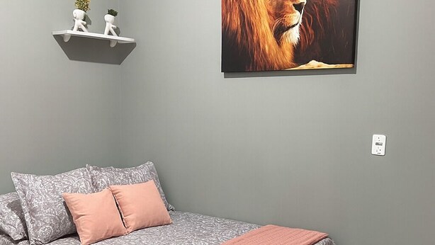 Une chambre à coucher avec un lit, une étagère fixée au mur ornée d’objets décoratifs et un tableau encadré représentant un lion.