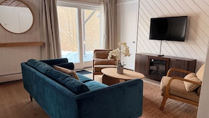 Ein Wohnzimmer mit einem blauen Sofa, einem Holztisch, einem Sessel, einem Fernseher und einem Kamin.