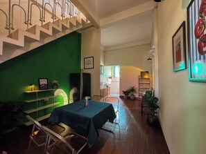 A dining area with a table set for two, a green wall, and a staircase. - XOM House - House in Pleiku (Pleiku)