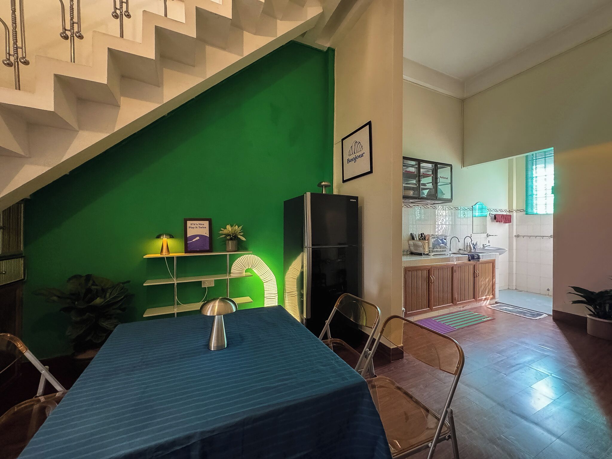 Een eethoek met een tafel, stoelen, een groene wand, een keuken met kasten en een trap.