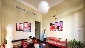 Ein modernes Wohnzimmer mit einer Couch, einem gemusterten Teppich, einer weißen Lampe, einer roten Bank und zwei an der Wand befestigten Bildern.
