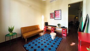 Ein Wohnzimmer mit braunem Sofa, einem Teppich in Blau und Rot, einer weißen Stehlampe, einem roten Schrank und einer Wandregal mit Dekoration.