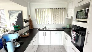 Una cocina moderna con armarios blancos, encimera negra y ventana con persianas.