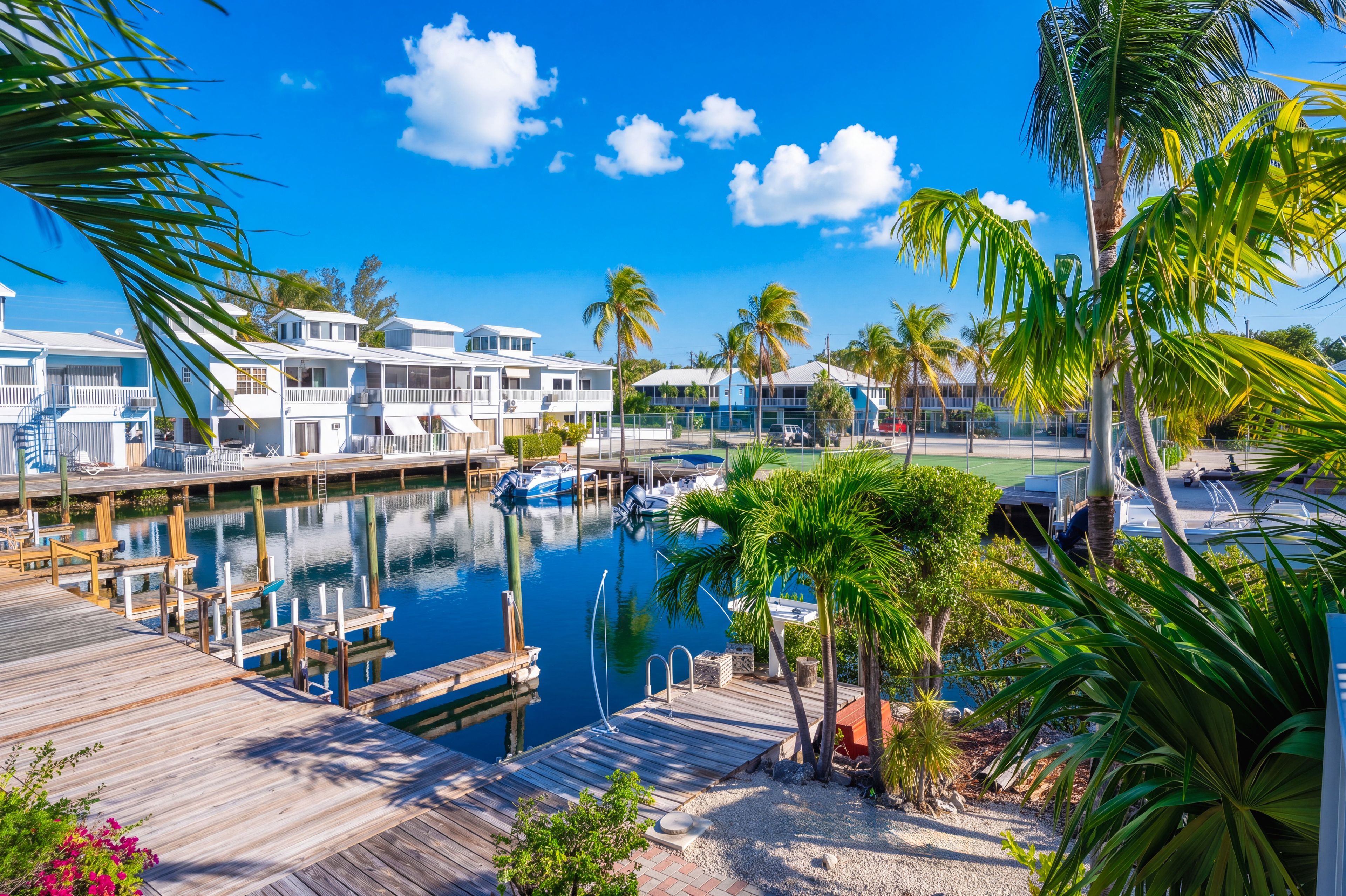 Ein Yachthafen mit vertäuten Booten, eine Holzsteganlage und eine Reihe weißer Gebäude mit Balkonen.