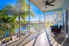 Ein Balkon mit Blick auf einen Pool und Palmen, einem Deckenventilator und Gartenmöbeln.