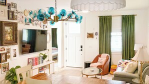 Ein Wohnzimmer mit einem Holzesstisch, weißen Stühlen, einem Sofa, einem Fernseher und einer Chandelier.