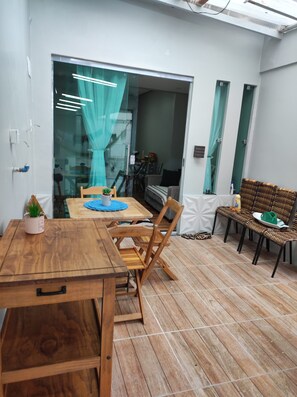A modern dining area with a wooden table and chairs, a glass partition with curtains, and a view of a balcony.