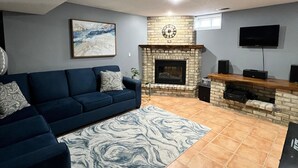 A living room with a blue sofa, a patterned rug, a fireplace, and a television mounted on the wall. - Beautiful basement (Wilmot)