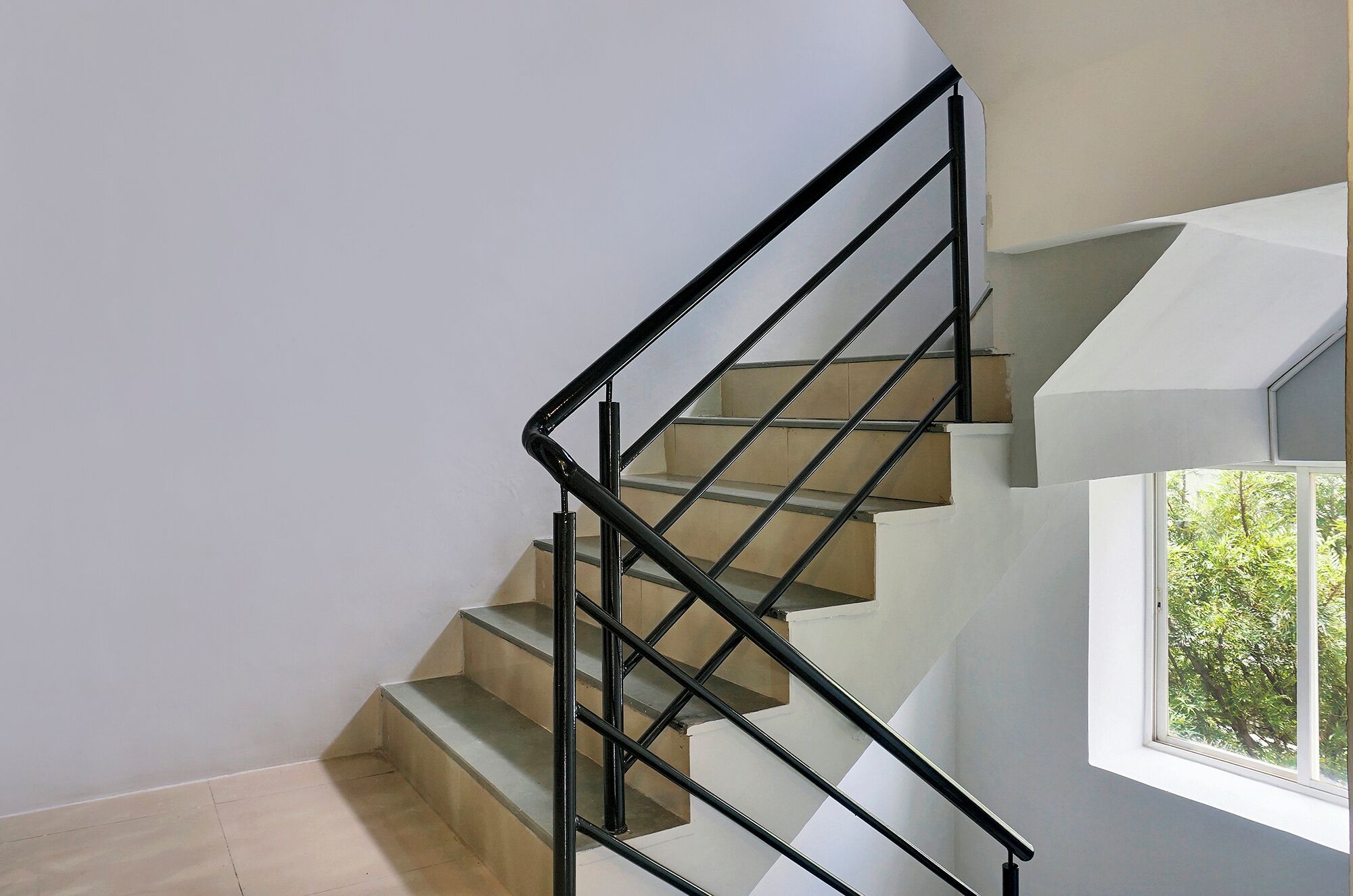 A modern staircase with black metal railings and beige steps, leading to a room with a large window.