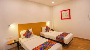 Une chambre d’hôtel avec deux lits, chacun agrémenté d’une couvre-lit colorée et de coussins blancs. On y trouve une petite table de chevet avec un téléphone et une lampe. La chambre est dotée d’un plancher en bois et d’un ventilateur de plafond.