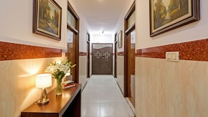 A hotel hallway with framed paintings on the walls, a reception desk with a lamp and flowers, and a door at the end. - Fabhotel Kg Palace (New Delhi)