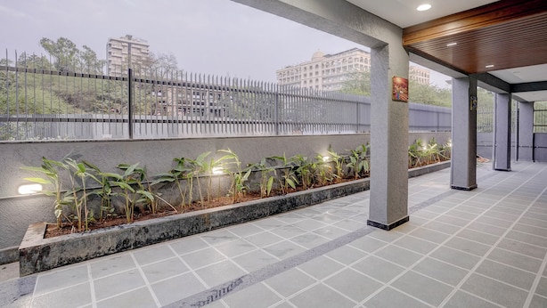 Um espaço ao ar livre coberto com piso de azulejos, um vaso de concreto baixo com plantas verdes e uma cerca de metal.
