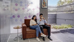 Uma área de estar moderna e interna com um sofá e uma mesa pequena, uma divisória de vidro com padrões hexagonais e uma pintura na parede.