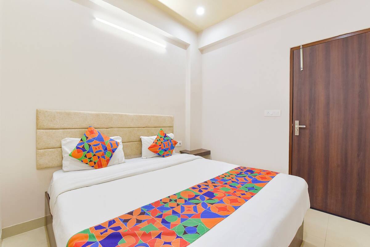 A hotel room with a bed, a wooden door, and a nightstand with a lamp.