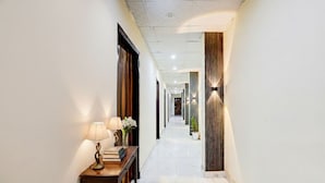 A hotel hallway with a marble floor, wooden paneling on the walls, and a table with a lamp and books. - Fabhotel The Galaxy (Faridabad)