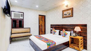 A neatly arranged bedroom with a bed, bedside table, lamp, and a television mounted on the wall. - Fabhotel The Galaxy (Faridabad)