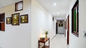 A hallway with framed landscape paintings, a wooden table with books and a vase of flowers, and a door at the end. - Fabhotel Sehrawat (New Delhi)