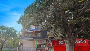 A building with a storefront, a tree in front, and a red gate. - Fabhotel The Royal Inn I (New Delhi)