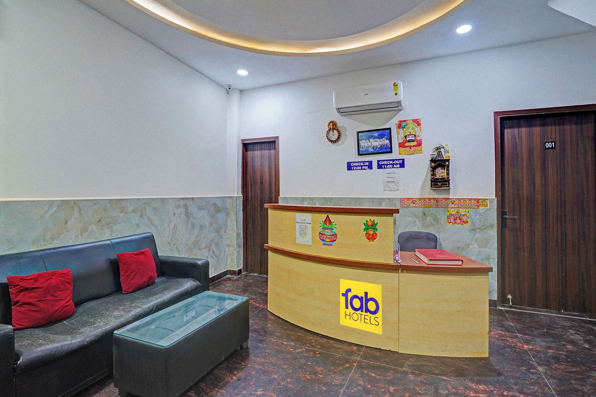 A hotel reception area with a reception desk, a sofa with red cushions, and a clock on the wall.