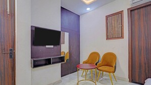 A room with a TV mounted on the wall, two chairs, a small table, and a wardrobe. - Via Stars (Noida)