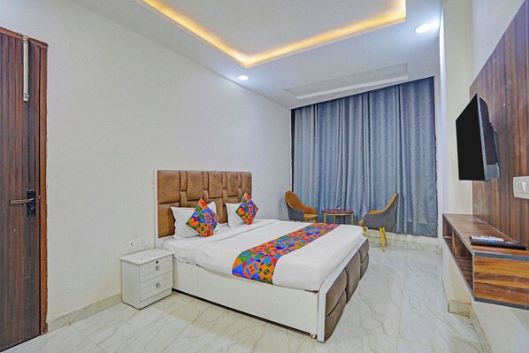A modern bedroom with a bed, nightstand, chairs, and a TV. - Via Stars (Noida)