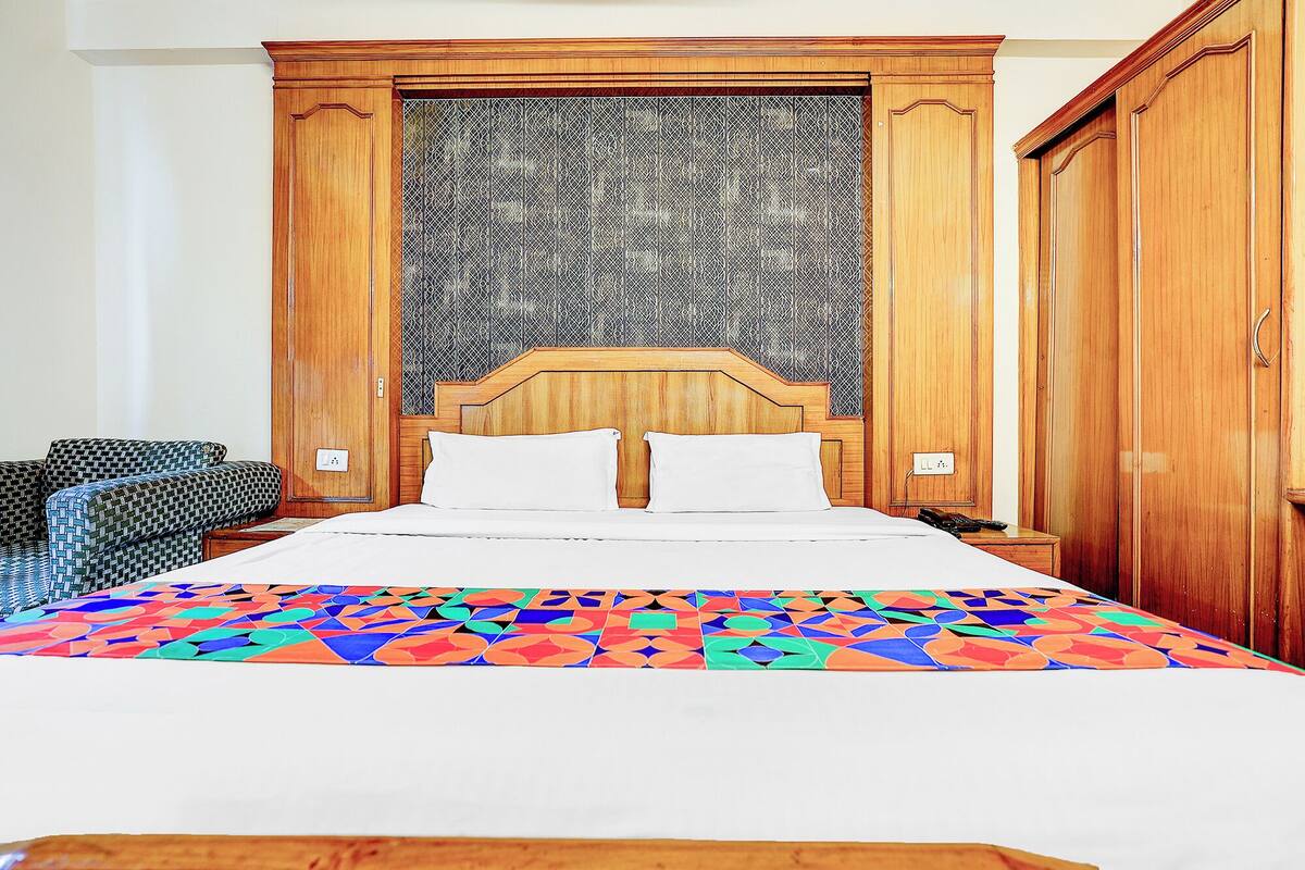 A hotel room with a bed, a wooden wardrobe, and a patterned wall.