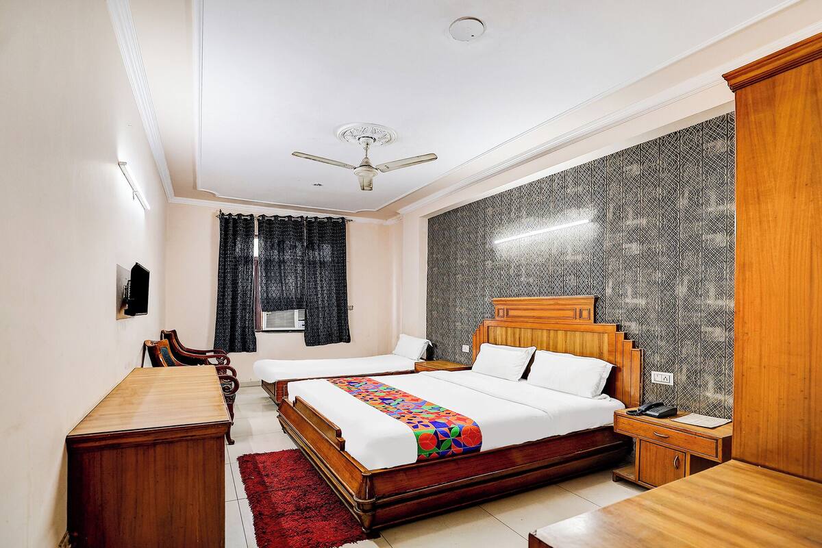A bedroom with a large bed, a wooden nightstand, a desk, a red rug, a ceiling fan, and a patterned wall.