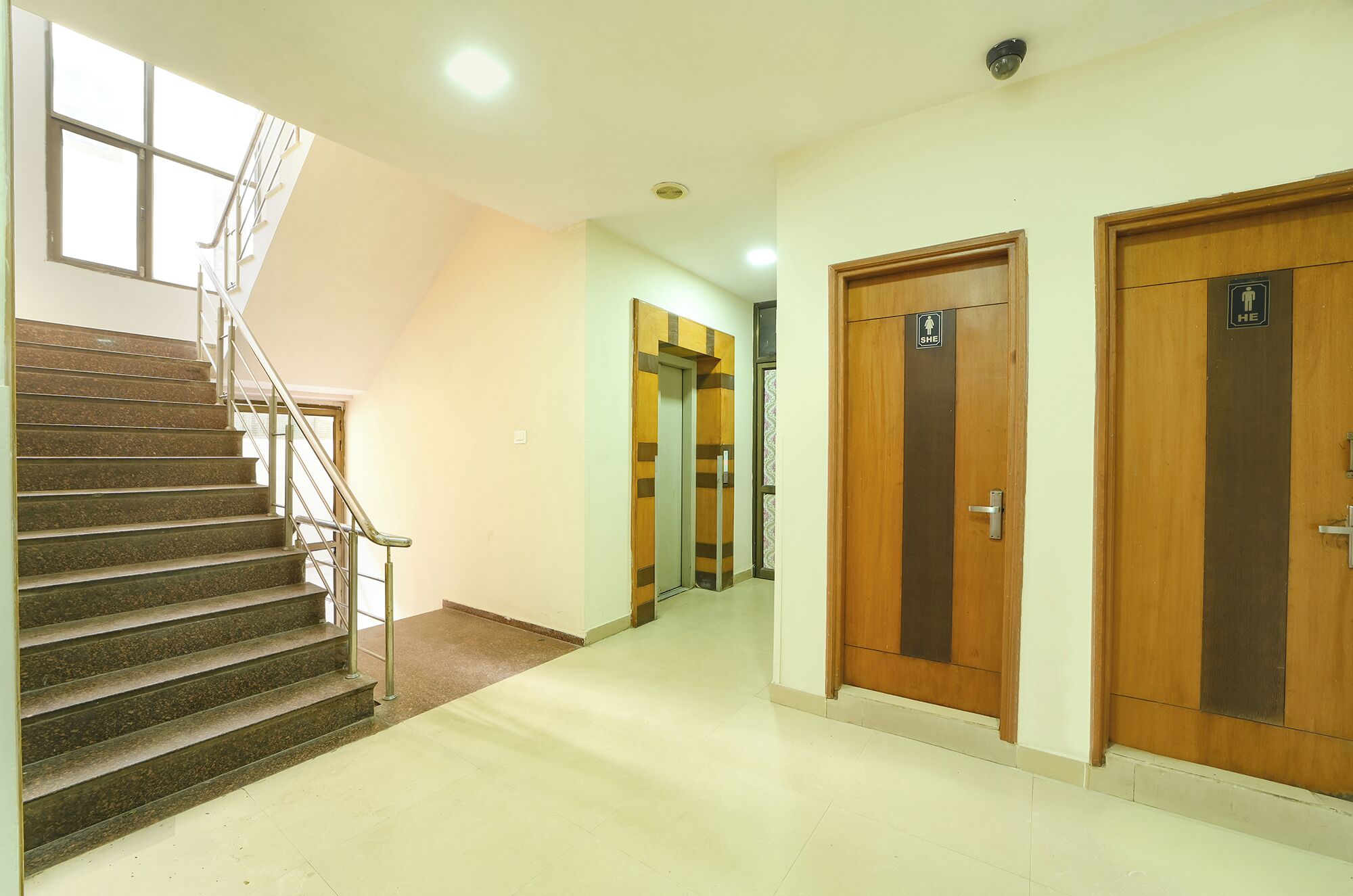A hotel corridor with a staircase, wooden doors, and a security camera.