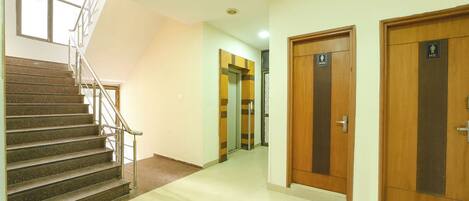 A hotel corridor with a staircase, wooden doors, and a security camera.