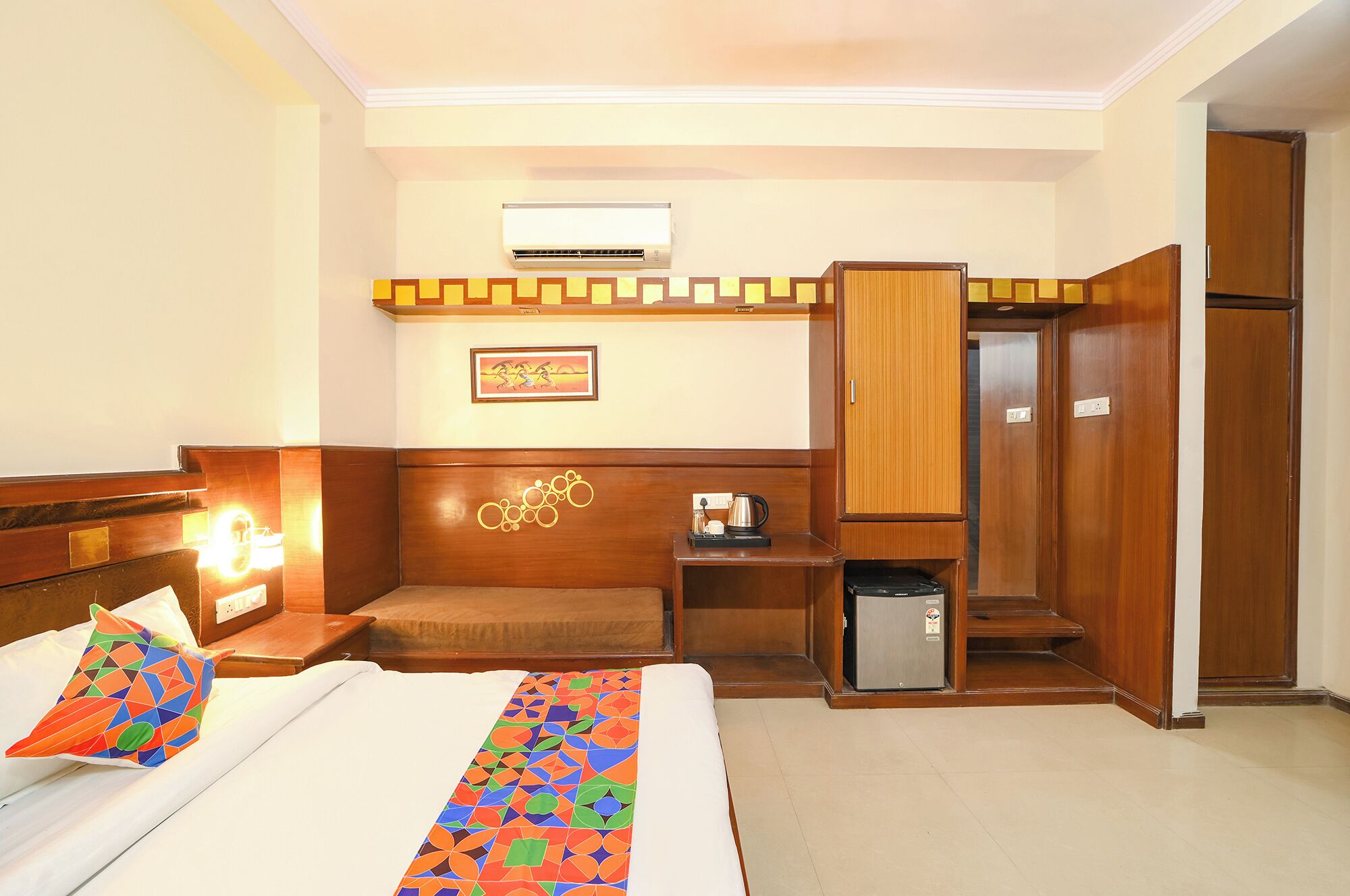 A hotel room with a bed, a desk, an air conditioner, a wardrobe, and a small cabinet.