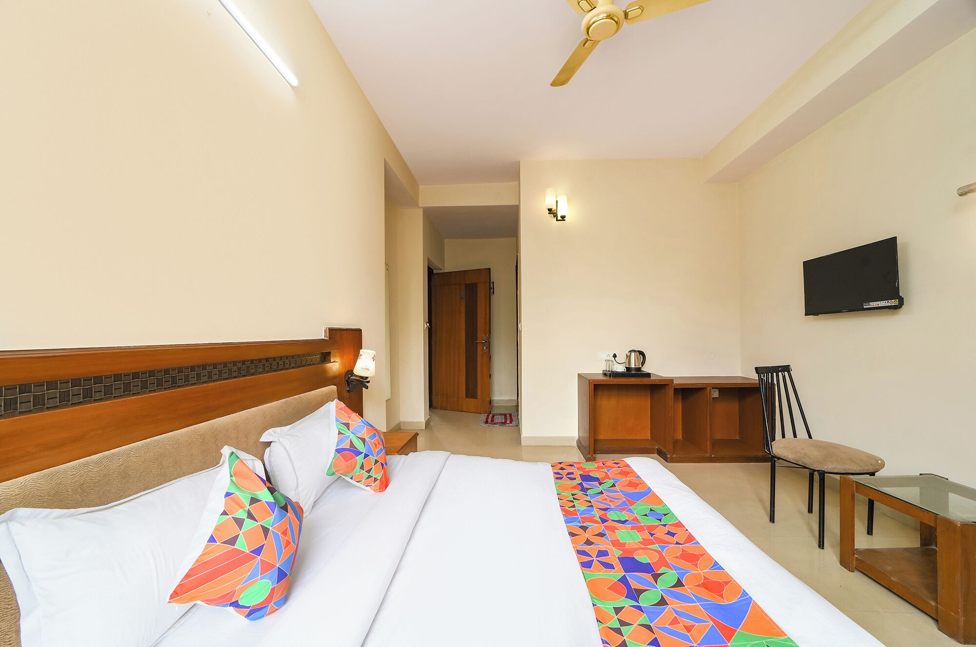 Ein Hotelzimmer mit Bett, Schreibtisch, Sessel, Fernseher und Deckenventilator.
