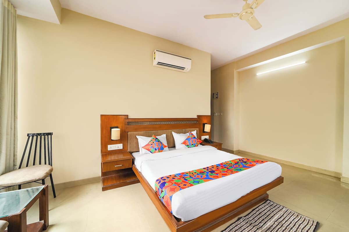 A hotel room with a wooden bed, a nightstand, a chair, a ceiling fan, and an air conditioning unit.
