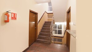 Una escalera con barandilla, un extintor en la pared y una puerta con placa numérica.