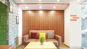 Un área de espera moderna con un sofá de cuero marrón, una pared con listones de madera y un mostrador de recepción.